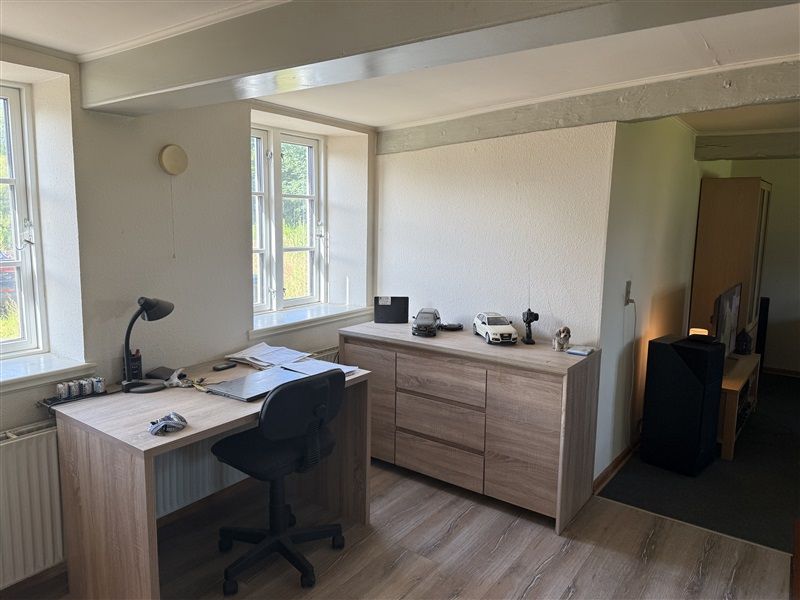 Et værelse med en høj bjælkeloft og lyseruder, der giver masser af naturlys og udsigt til grønne træer og et rødt bilmodel