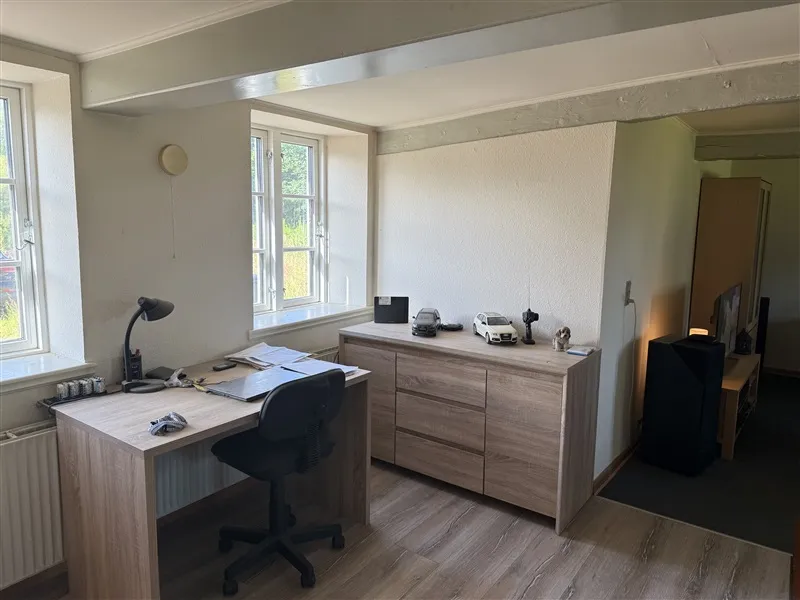 Et værelse med en høj bjælkeloft og lyseruder, der giver masser af naturlys og udsigt til grønne træer og et rødt bilmodel