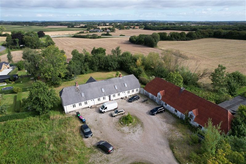 Flyfoto af et stort hus med to køretøjer parkeret udenfor og en husvogn parkeret lige foran