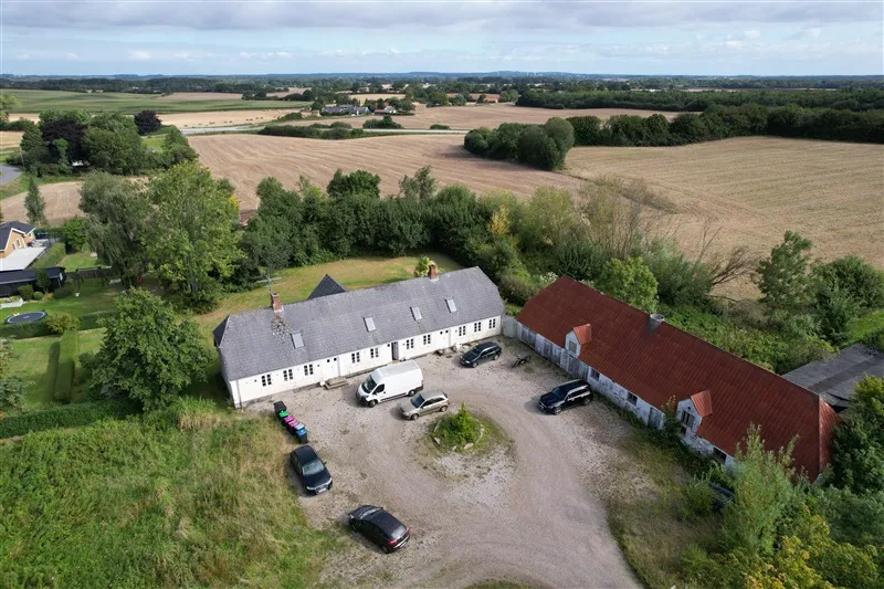 Flyfoto af et stort hus med to køretøjer parkeret udenfor og en husvogn parkeret lige foran
