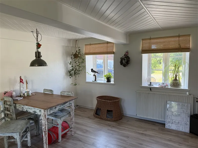 Foto af et køkken med lyse lofter, hængende lamper og vinduer med solblinder og udsigt til grønne træer