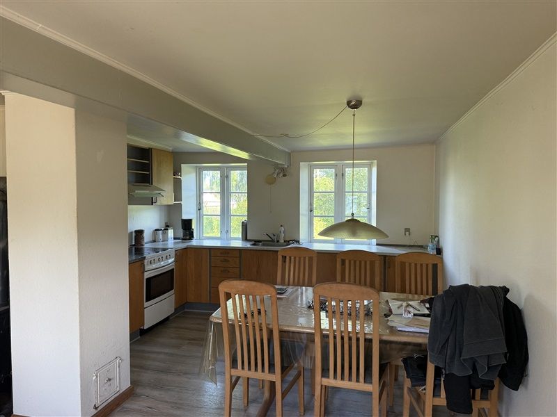 Velholdt køkken med moderne møbler, lyse vinduer og en stor spiseplads med plaskefri plastdæk og tøj på stolen