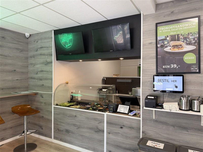 Køkken med rødt borde, skraldespande, computer og servietter samt et skilt med opskrift og pris