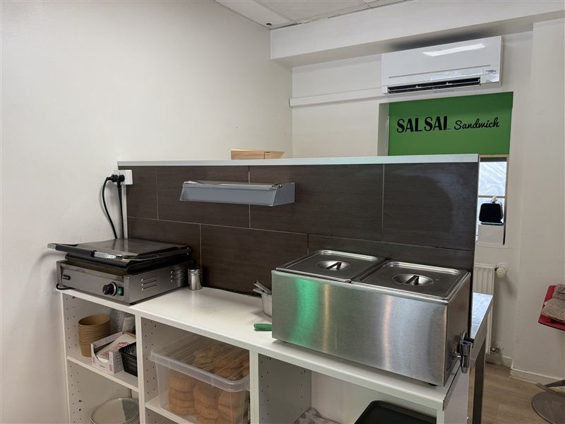 Moderne kommercielt køkken med grill og gryder samt hylder med sandwich og andre forsyninger.