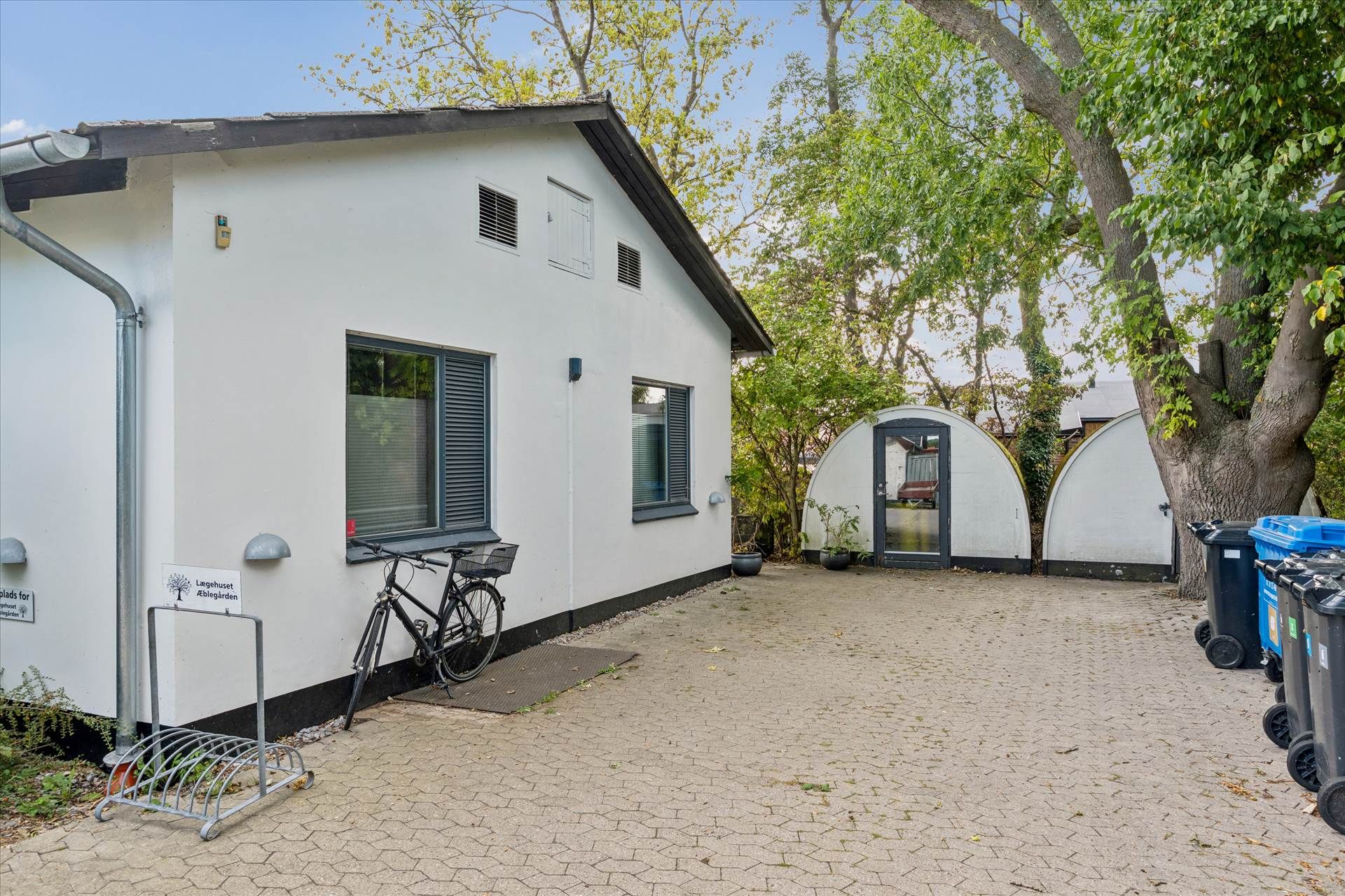 En hvid erhvervslejlighed med træk og vinduer i gården, der er udstyret med en cykelstander og skraldspande