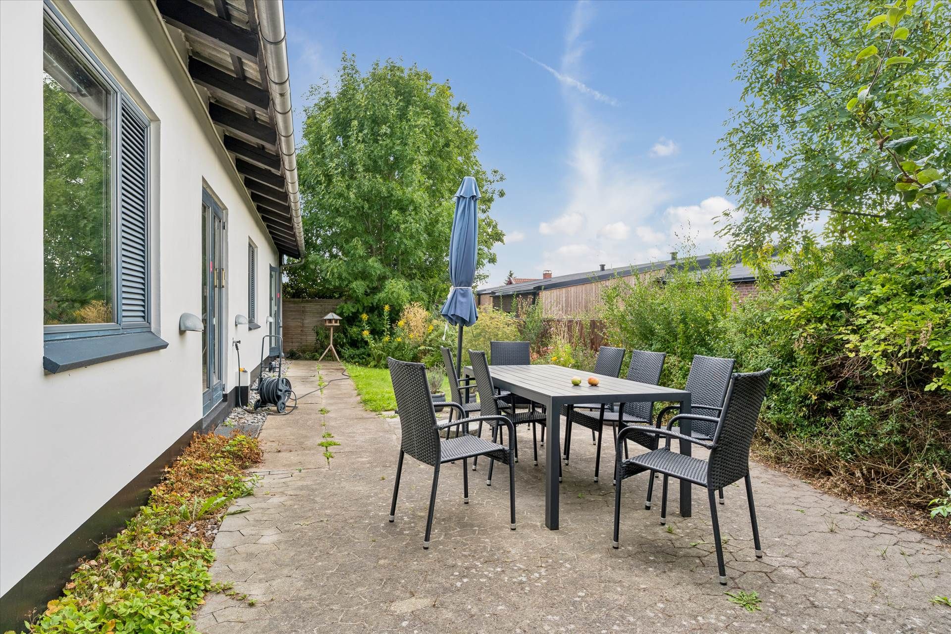 En terrasse med en lang bord, hvor der er placeret seks stole, og der er en paraply i spidsen