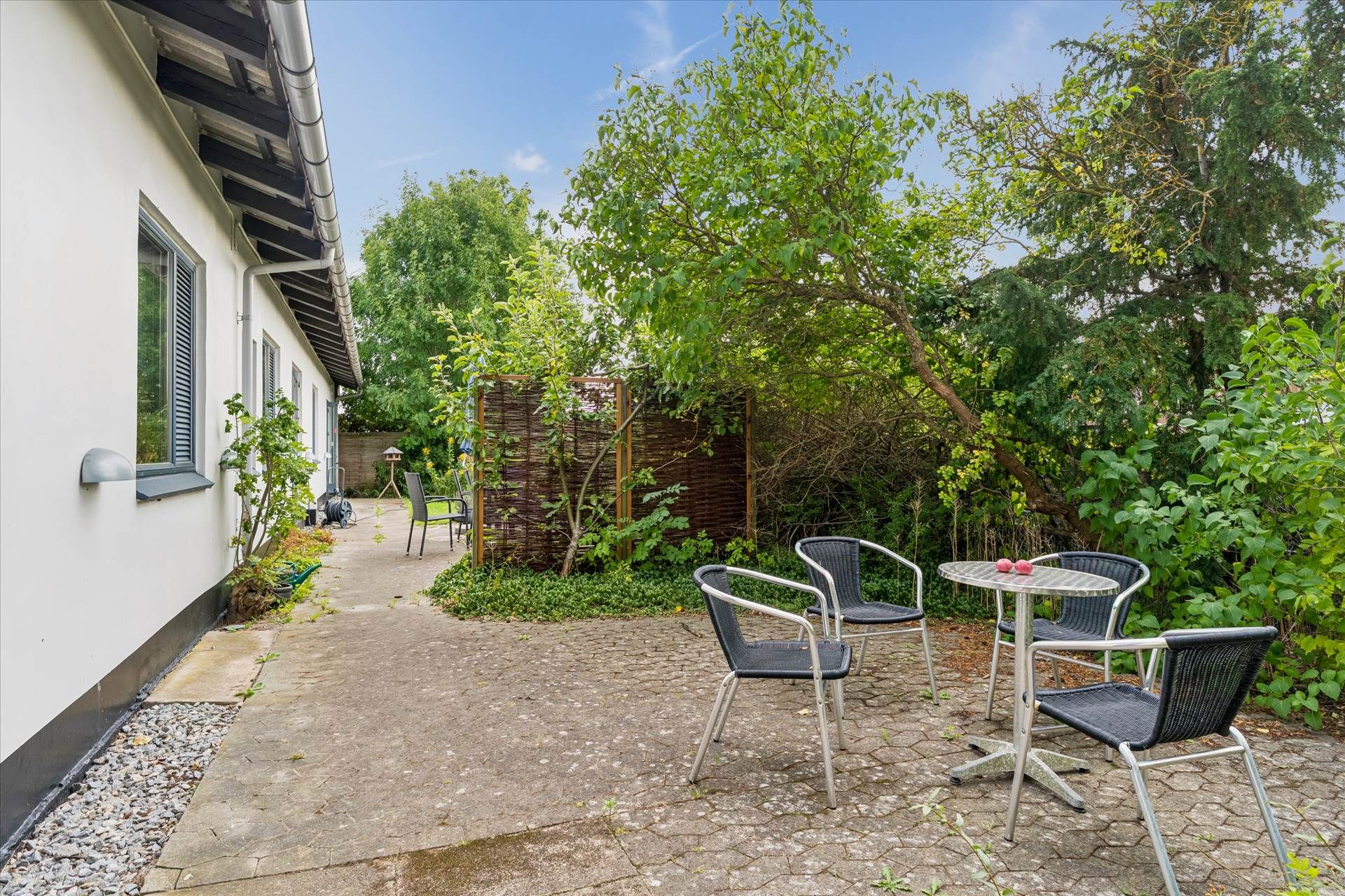 En have med en lille møbelgruppe, der består af et rundt bord og fire stole, samt en hvid bygning med en sollampe og et