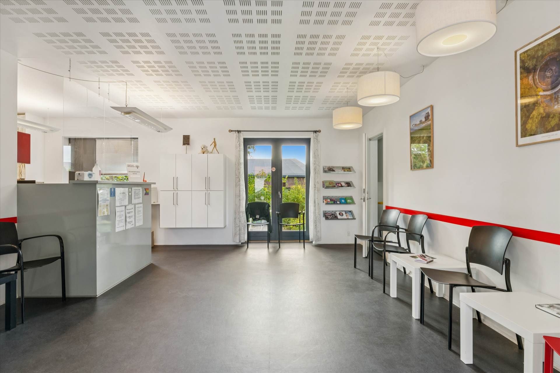 Inde i et lægehus med en stor, åben kontorlokal og hvide vægge med møbler og billeder