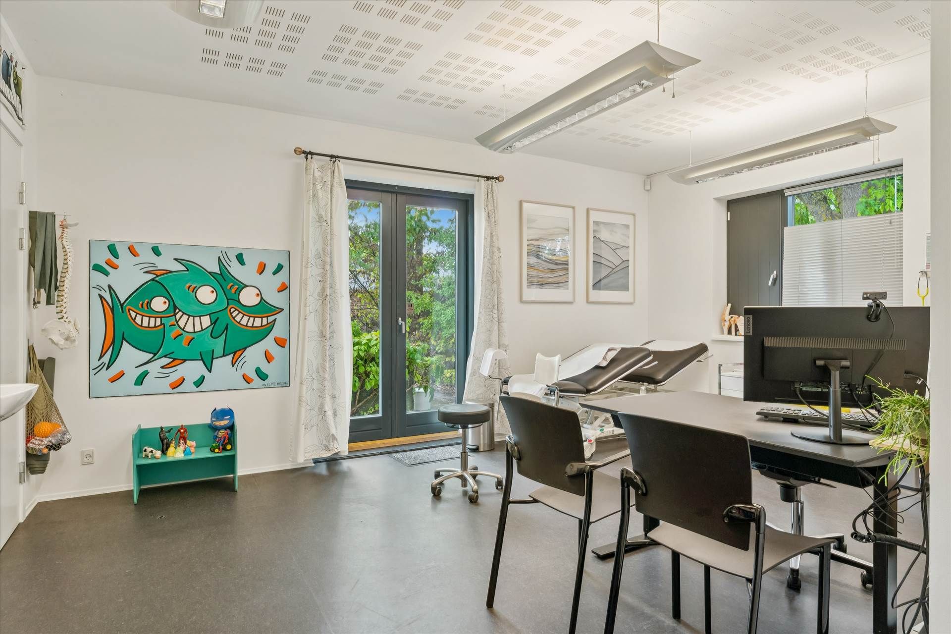 En lægepraksis med en stor åben dør og flere lægestuer med en stor computer og en række stole til patienter