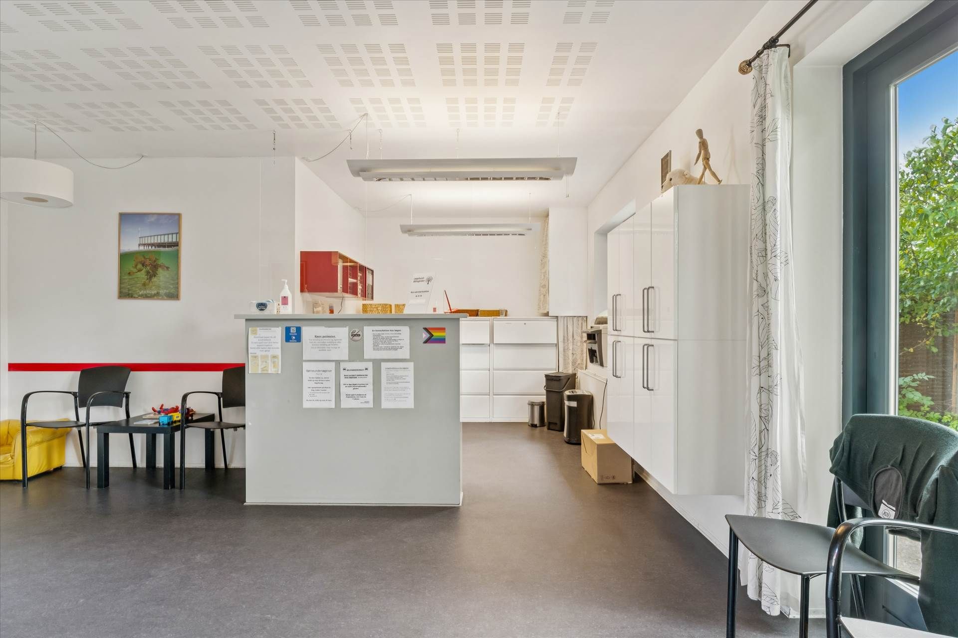 Minimalistisk kontorlokaler med højloft, hvide vægge, loftslampe og lysegul gulvbelægning. Et moderne skrivebord med