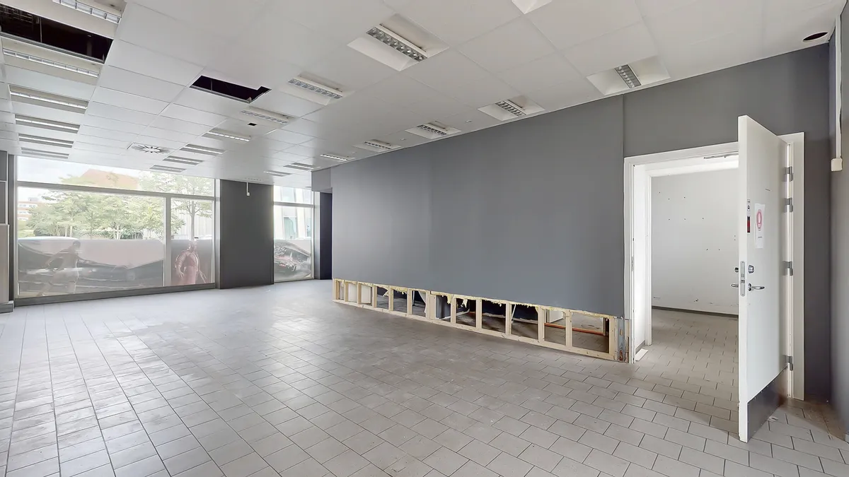 Et tomt kontorlokal med gulv og loft i lyse farver og store vinduer med udsigt til grønne træer og bygninger