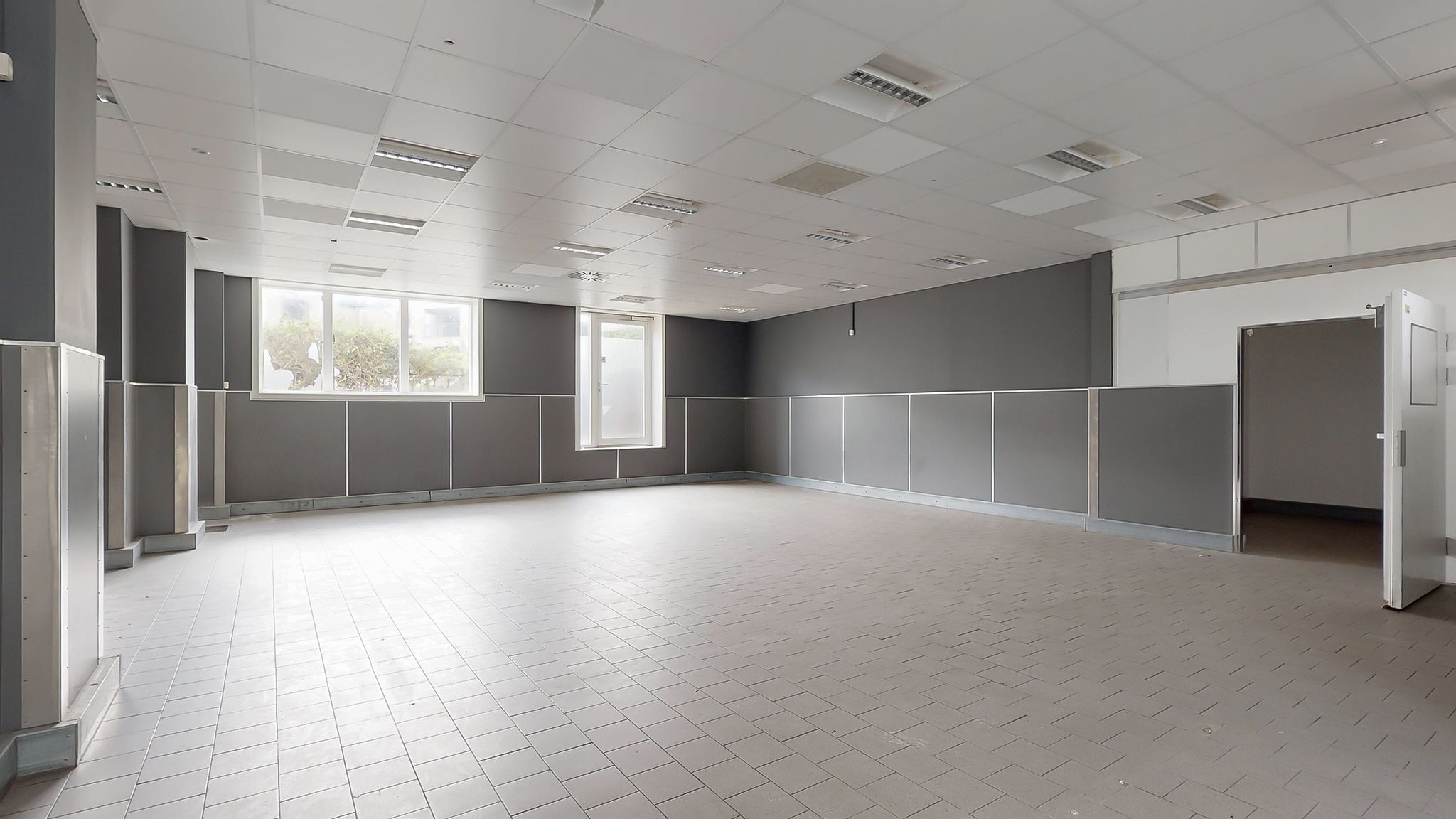 Et tomt lokale med hvide vægge og gulv samt grå vægge og loft med indbygget belysning