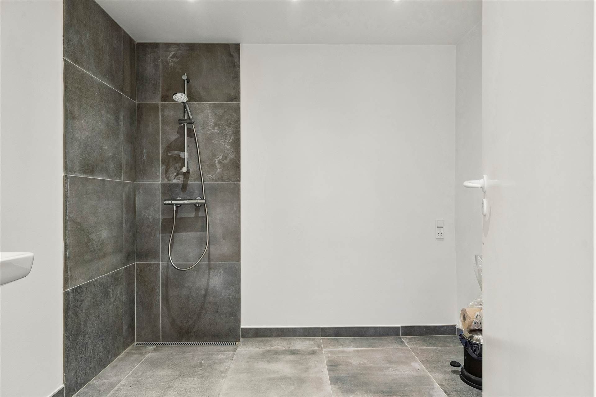 Et moderne badeværelse med en stor grå mur, en moderne grå badeværelsesbruser og en hvid væg med en dør og en