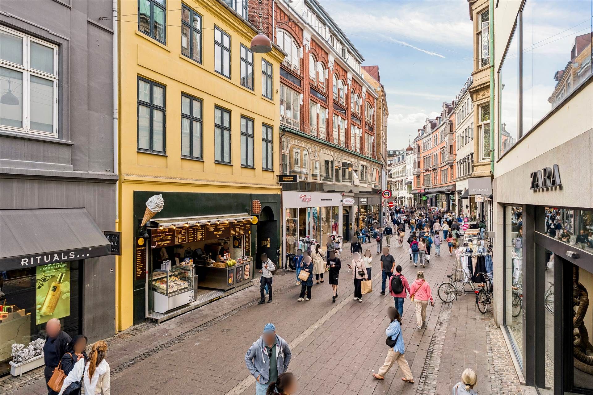 Flere mennesker vandrer rundt på gågaden Vimmelskaftet i København med flere butikker og høje bygninger i baggrunden