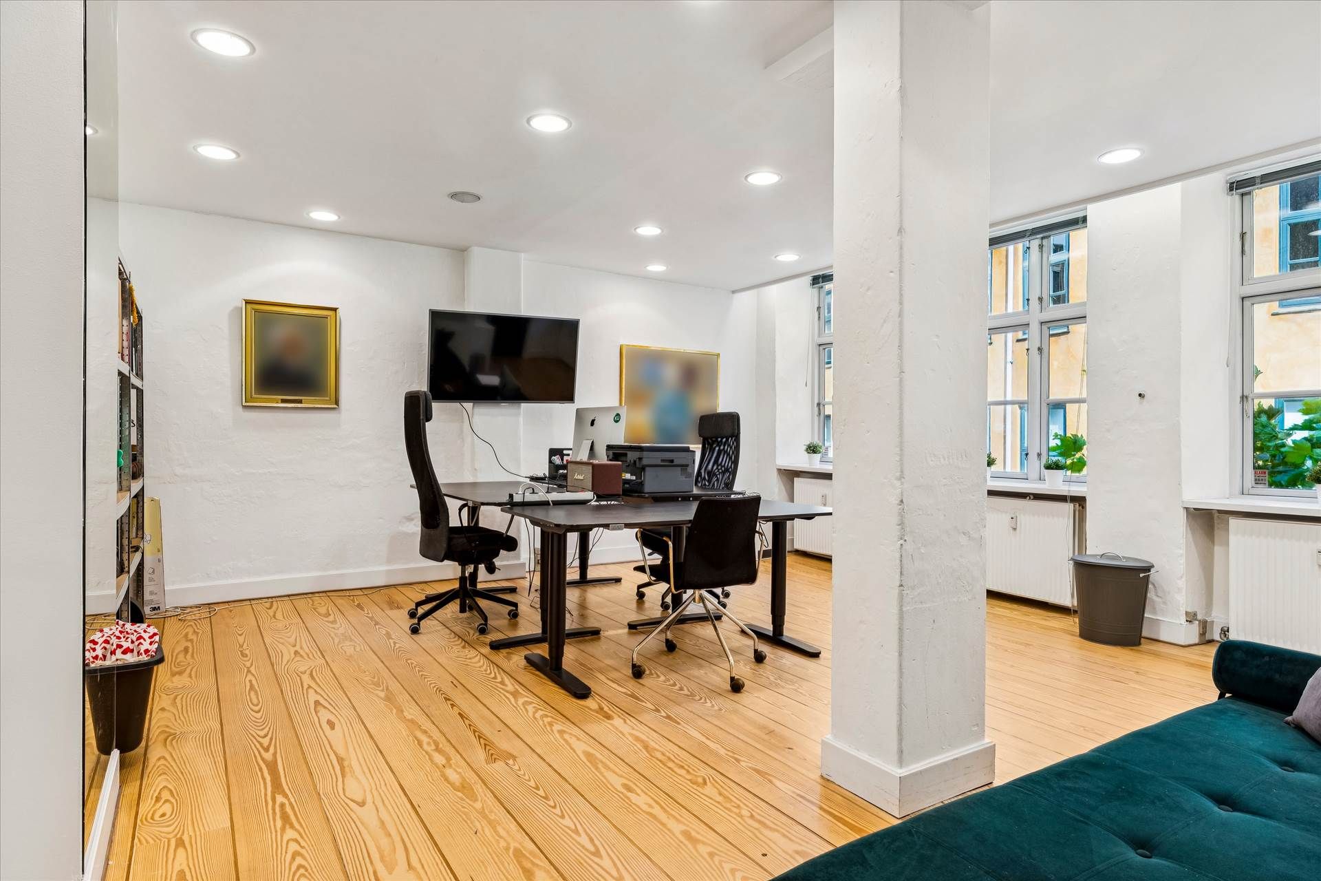 Et moderne kontor med højloft, skriveborde, stolene og en tv-skærm. Der er vinduer med udsigt til gade og planter på