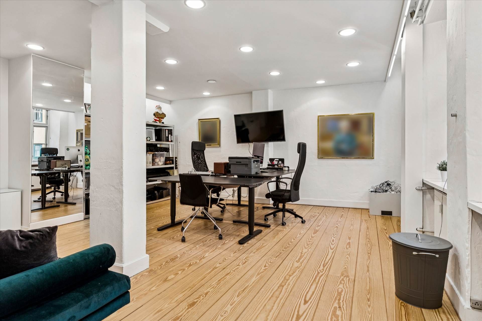 Kontor med skrivebord, stol, tv, computer og printer samt kunstværker på væggen og et spejl