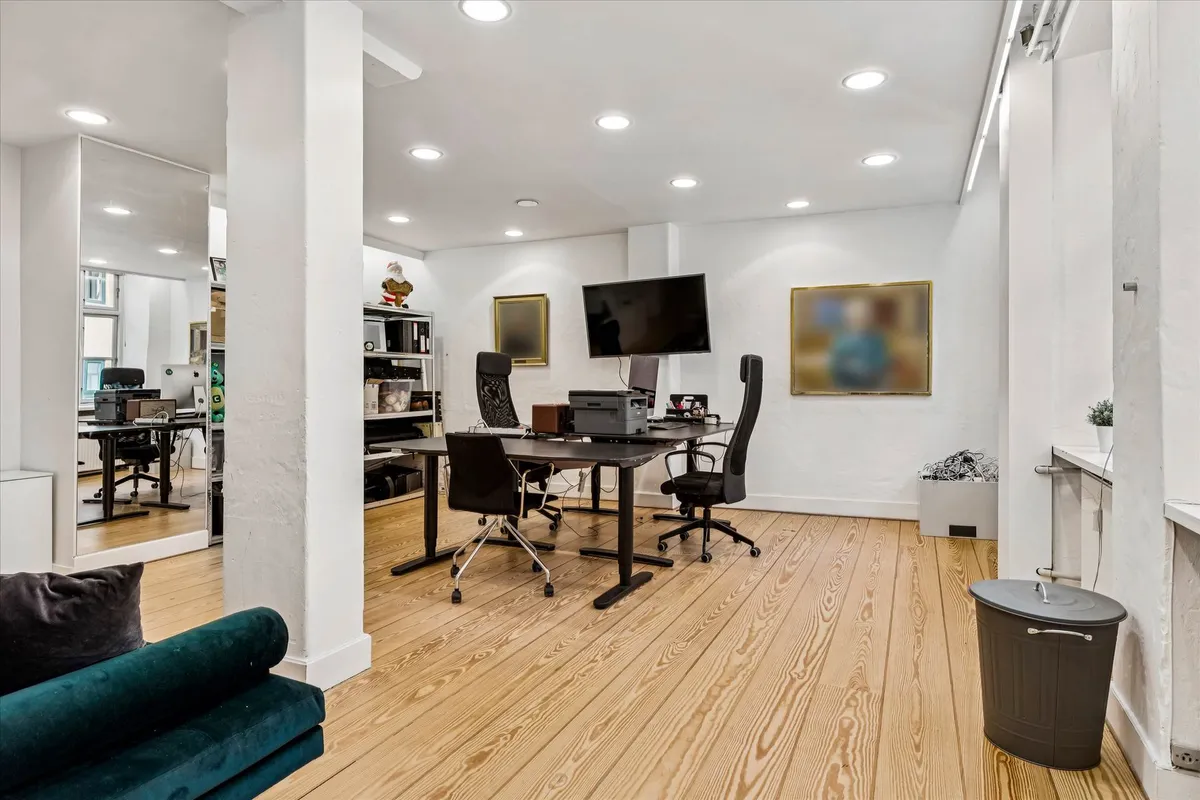 Kontor med skrivebord, stol, tv, computer og printer samt kunstværker på væggen og et spejl