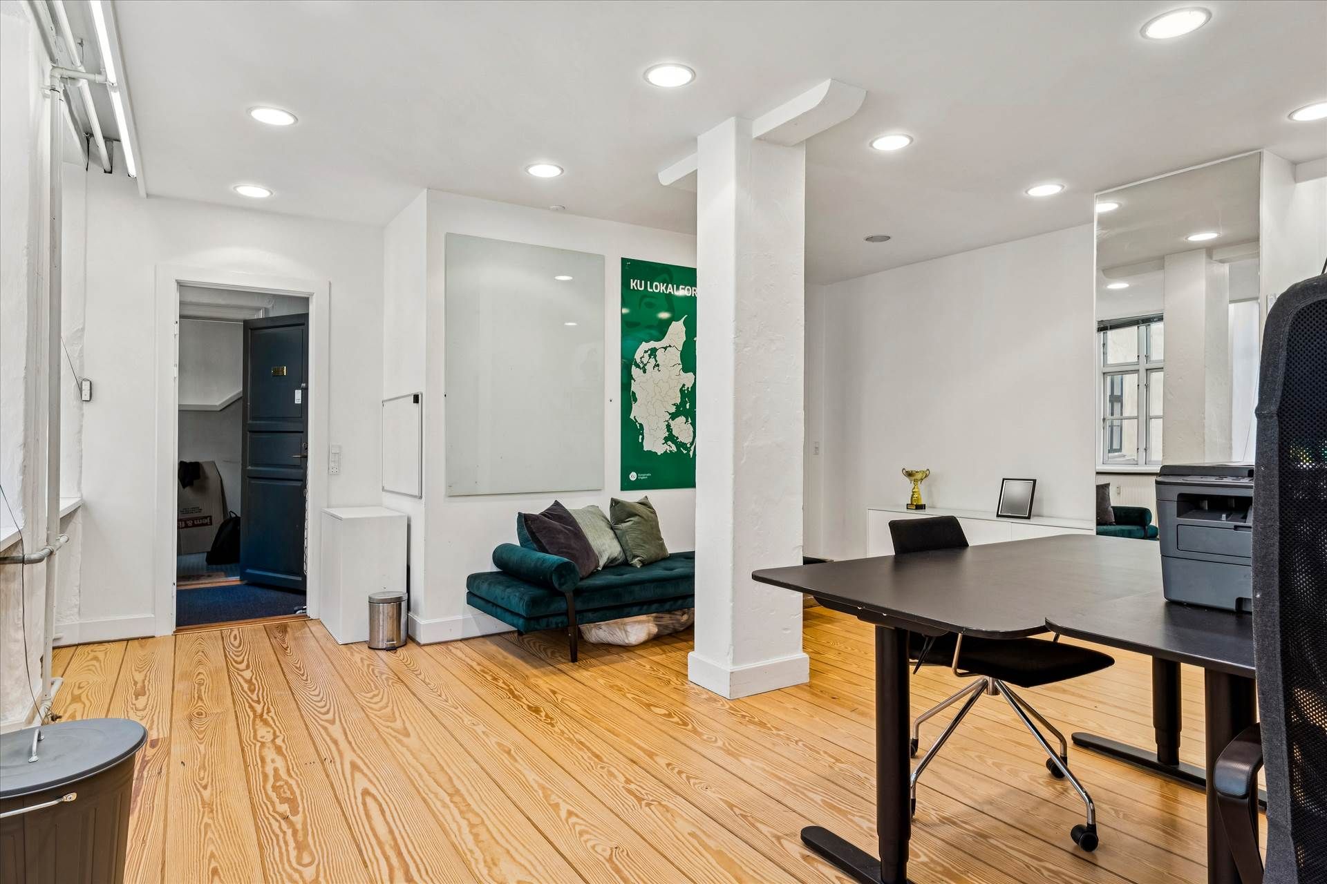 Moderne kontor med højloftede rum, trægulve, og et stort, grønt kort på væggen, der viser Ku Lokalfor. Et skrivebord med en