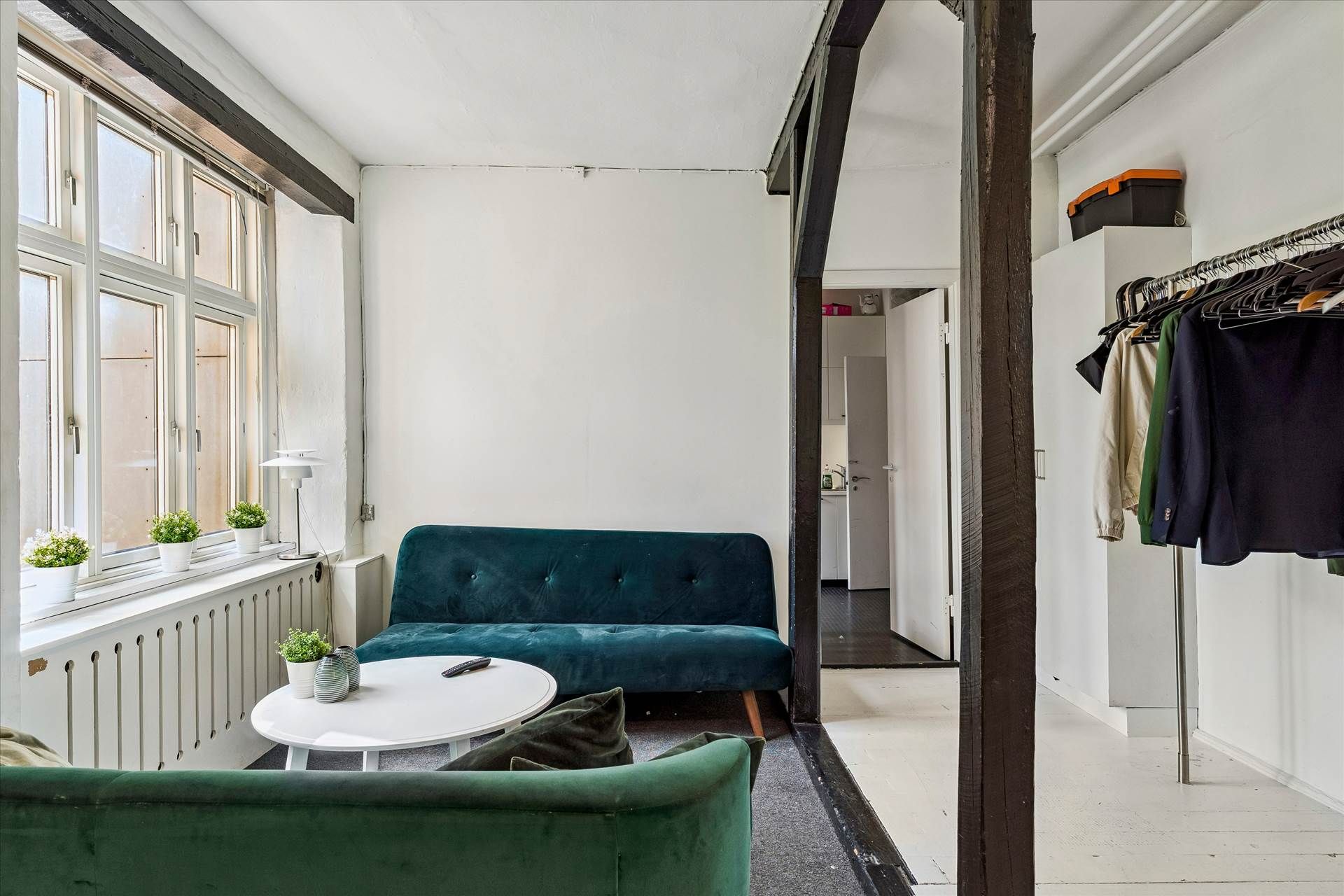 Et moderne og lyse interiør med to grønne sofaer, et hvidt rundt bord og en åben dør.