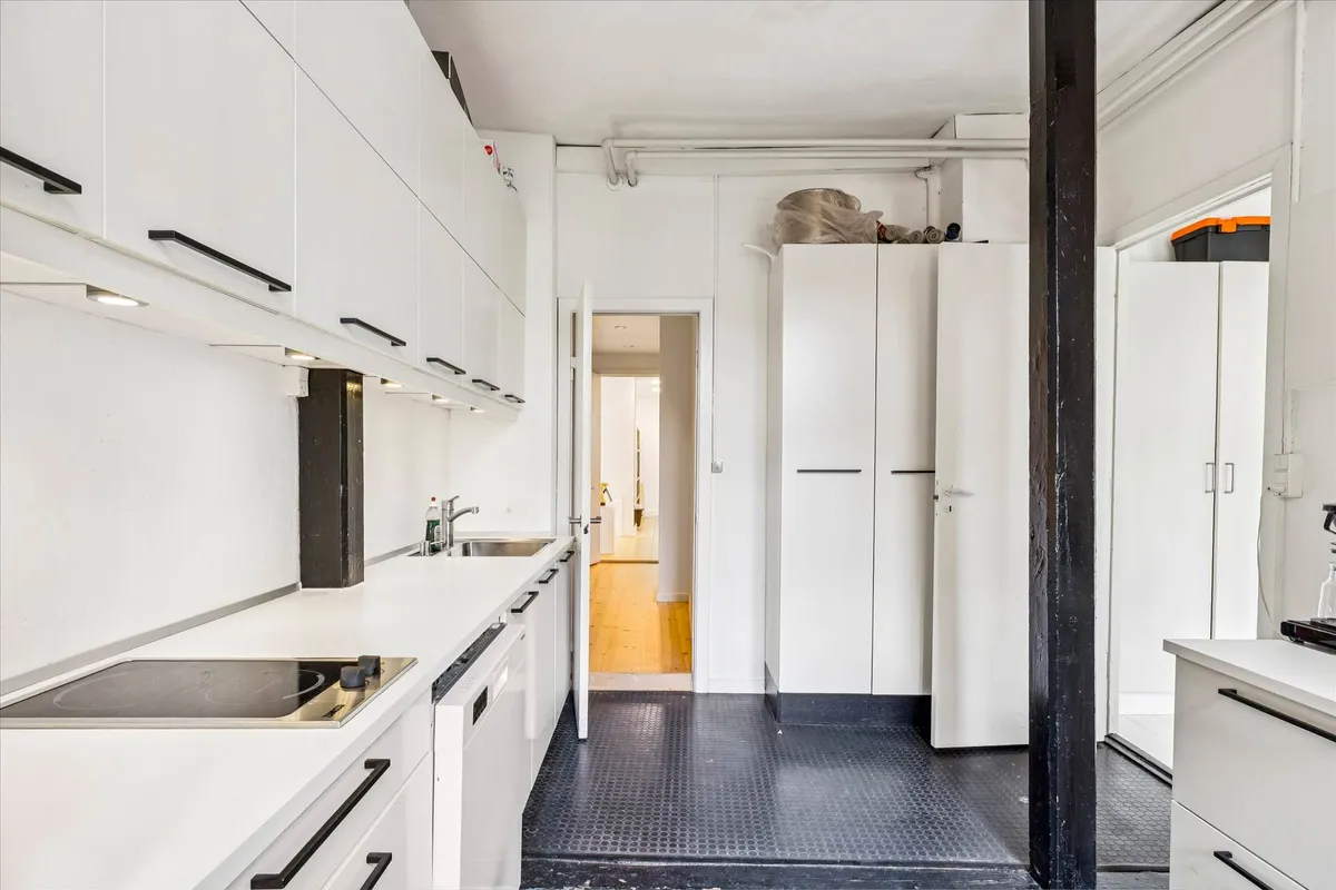 Minimalistisk designet køkken med hvide vægge og møbler samt en stor køkkenplade og moderne hætte over ovnen