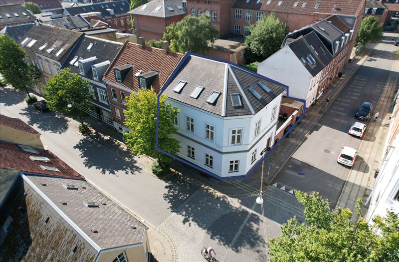 Kolding bymidte med mange bygninger, hvor en ejendom med røde tag og hvide vægge er fremhævet af et blåt felt