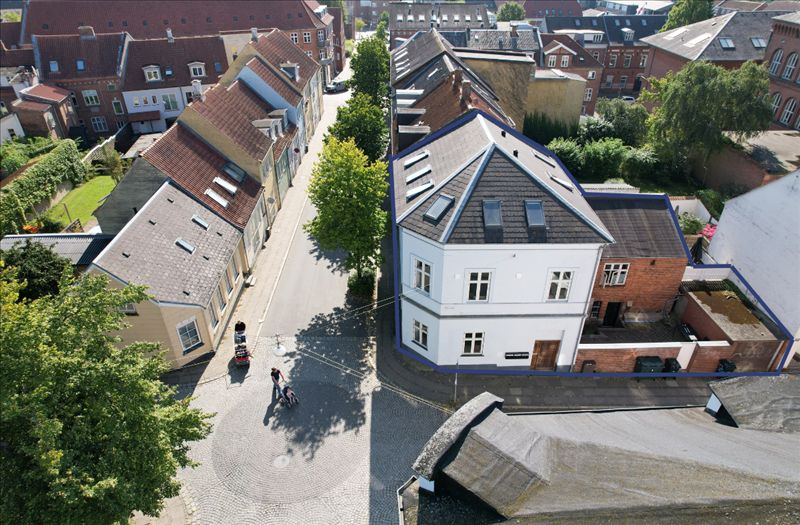 Koldings gade med røde tag, træer og to mennesker med barnevogne, og en ejendom med hvide vægge og brunt tag