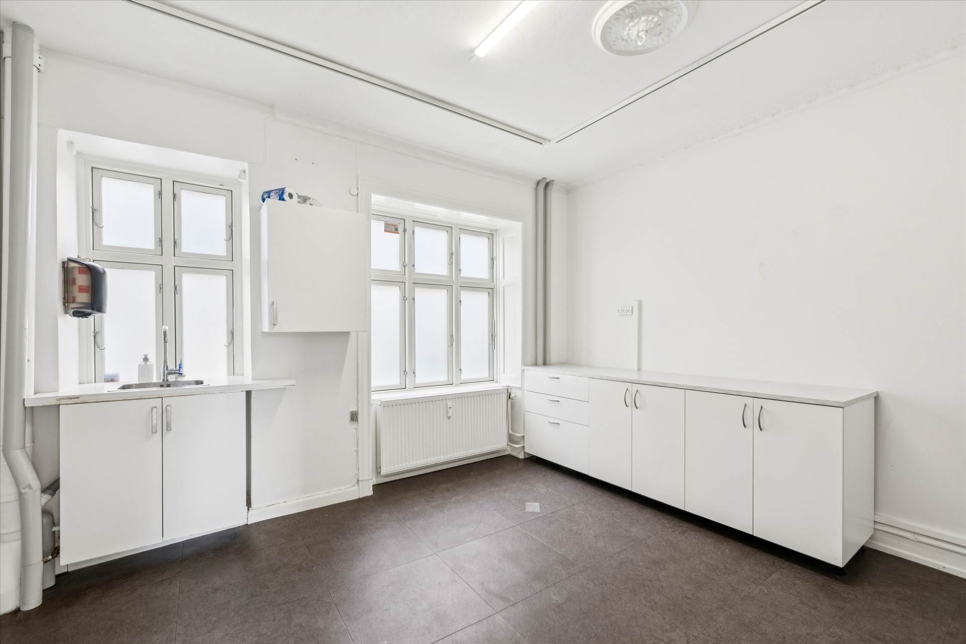 En ren og veludstyret køkkenafdeling med hvide vægge, møbler og gulv samt et vindue med glasruder.