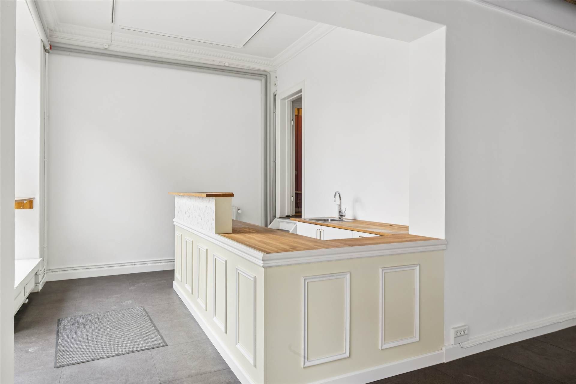 En ren og minimalistisk køkkenforhøjning med hvid maling og træ top, to hængeskabe, og en sink med vandhane