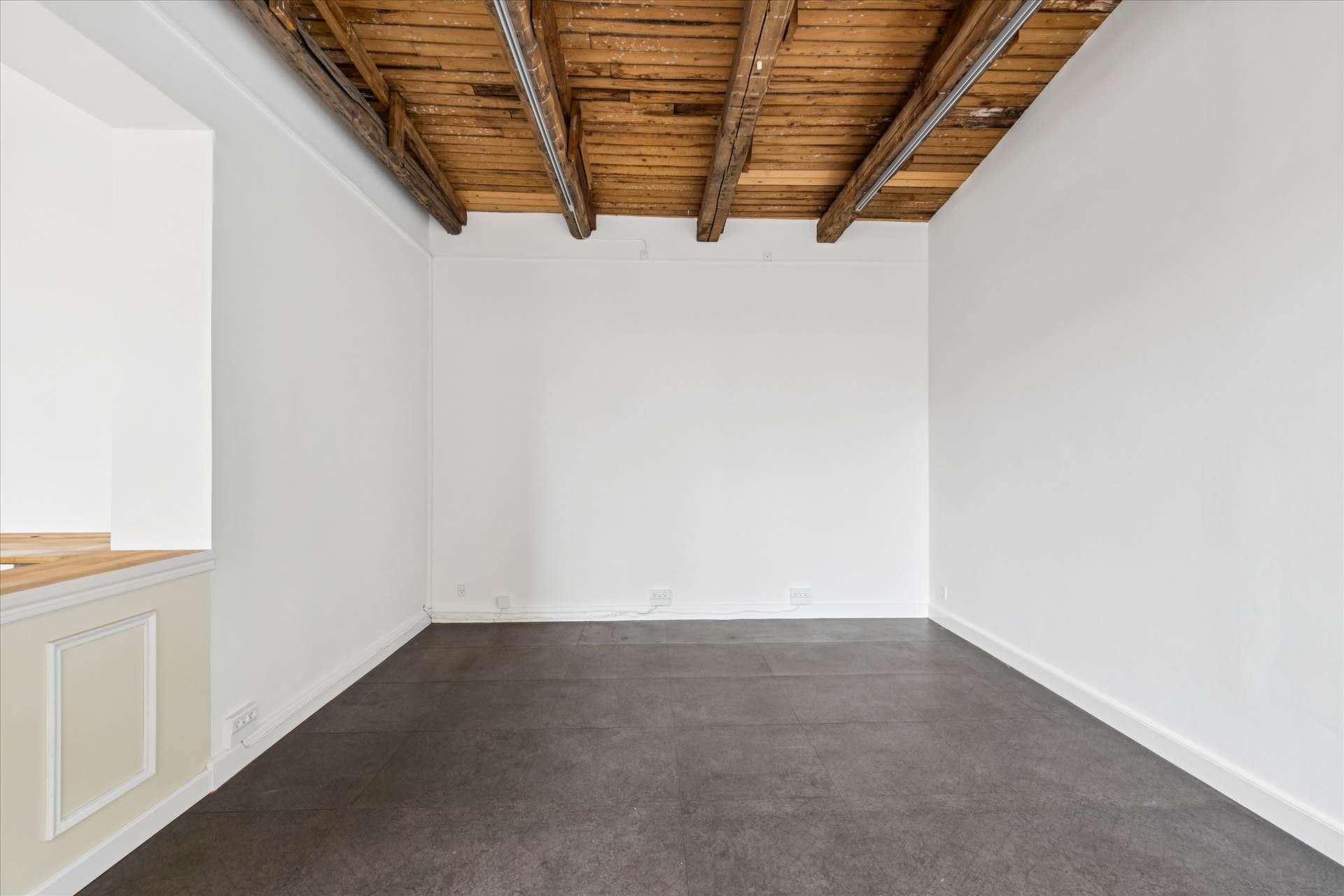 En tom og minimalistisk indretning med hvide vægge og gulv og en træloft. Foto taget fra gulvet op mod loftet med synlige