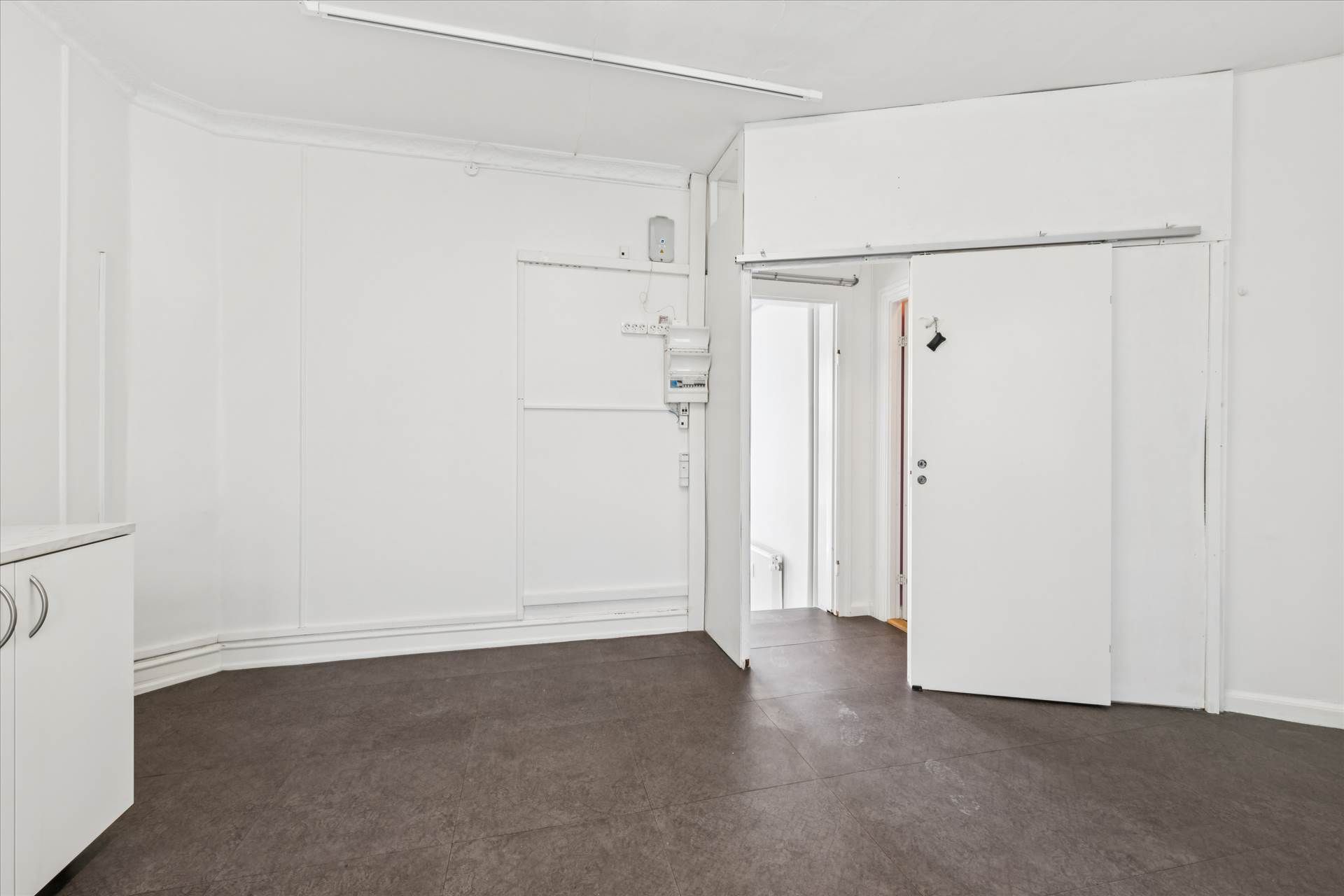 En stor, lys og ren stue med hvide vægge, gulv og loft samt en åben dør og vinduer