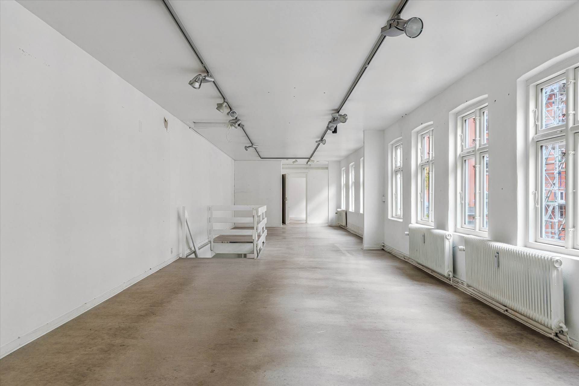 Langt og smalt erhvervslejemål med højloft, høj kvalitet og meget lys. Fire vinduer og lysekroner i loftet.
