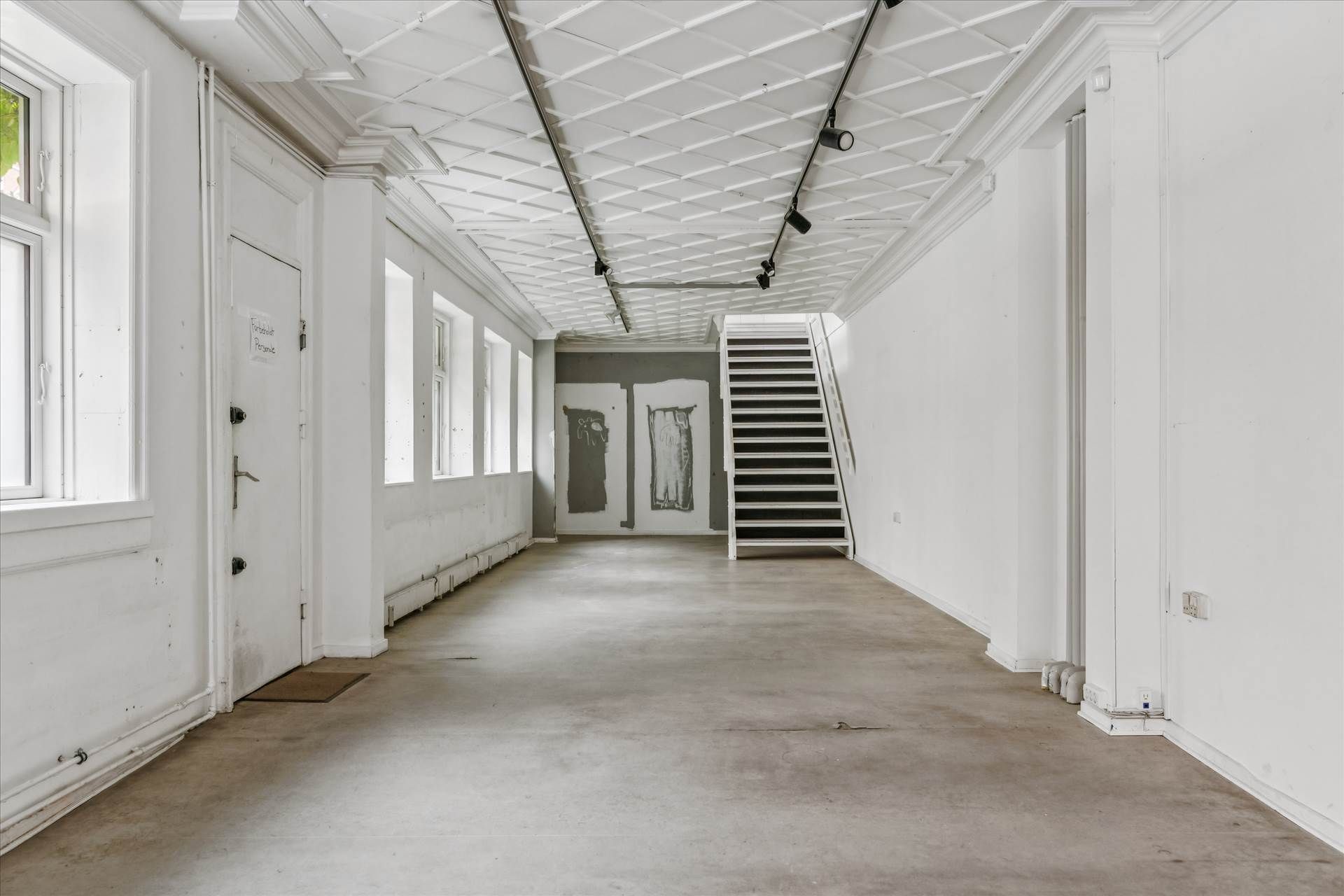 En hvid og lys hall med lyse lofter, højt ligger flere spotlights og gulvet er uden møbler og udsmykning