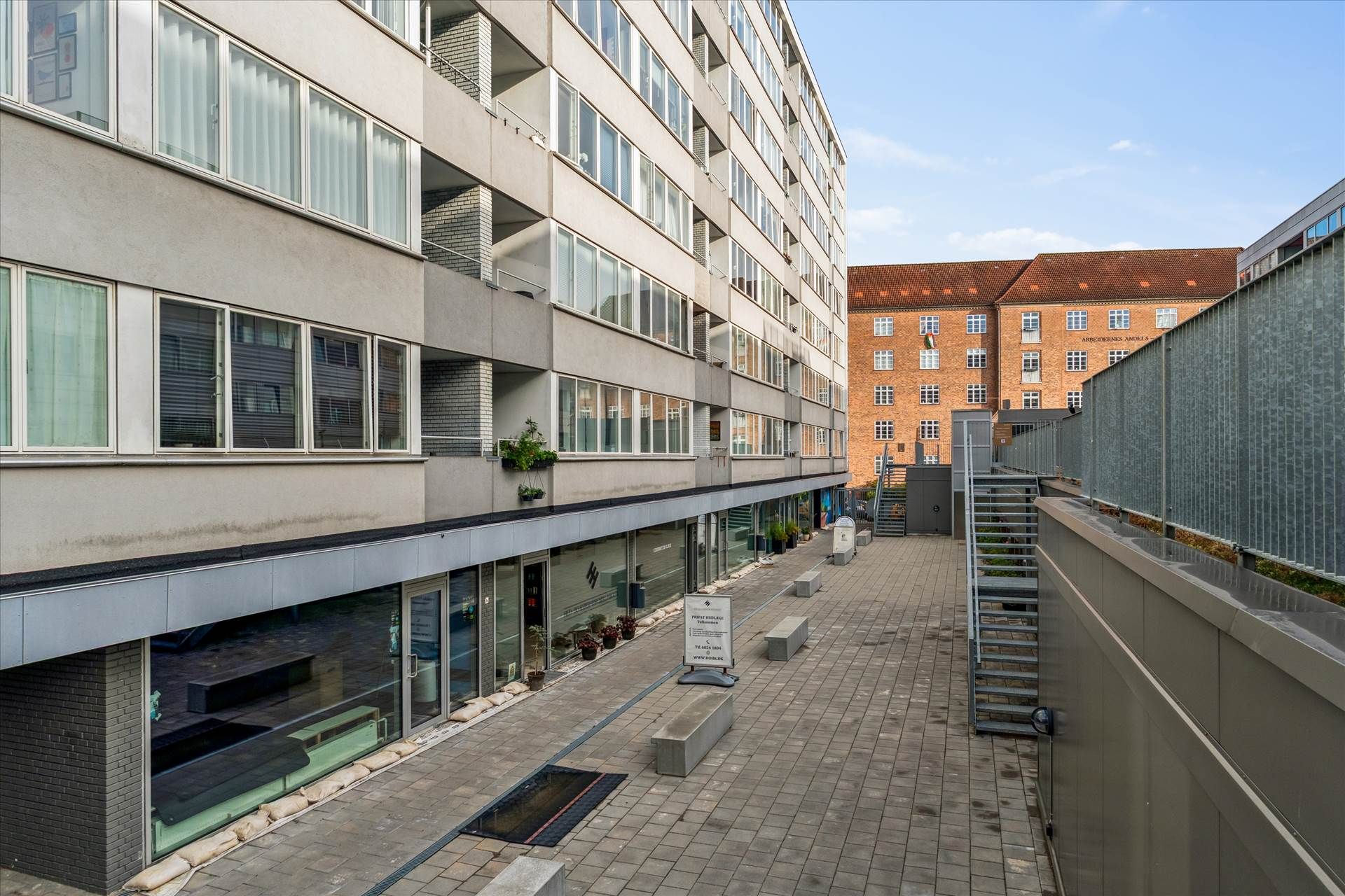 En moderne bygning med glasvinduer og terrasser i gården med en mur og et skrånende tag