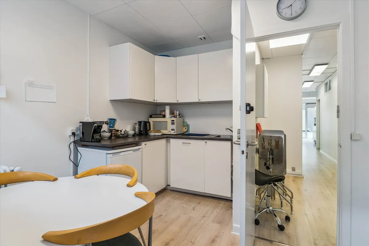 I et moderne køkken med hvide vægge og lyse lofter er der en hvid rund spisebord med to lysestole og en høj mikrobølgeovn