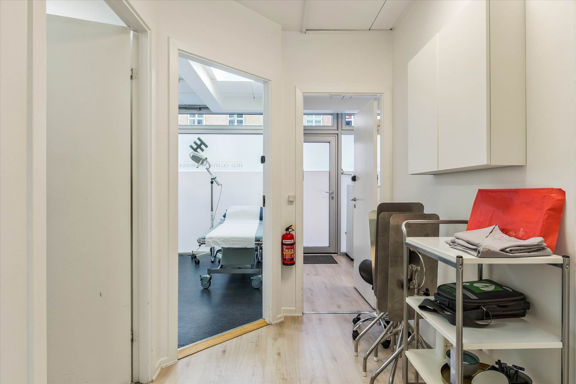 En lægeværelse med et hvidt lægebord, et højt sengekar, en hængeskab og en håndskur i en rolig og tilbagetrukket beliggenhed