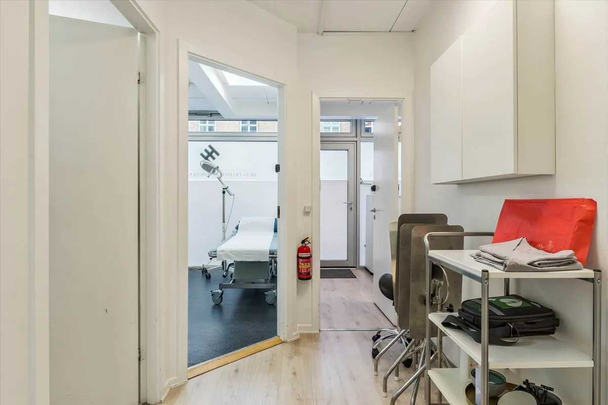 En lægeværelse med et hvidt lægebord, et højt sengekar, en hængeskab og en håndskur i en rolig og tilbagetrukket beliggenhed