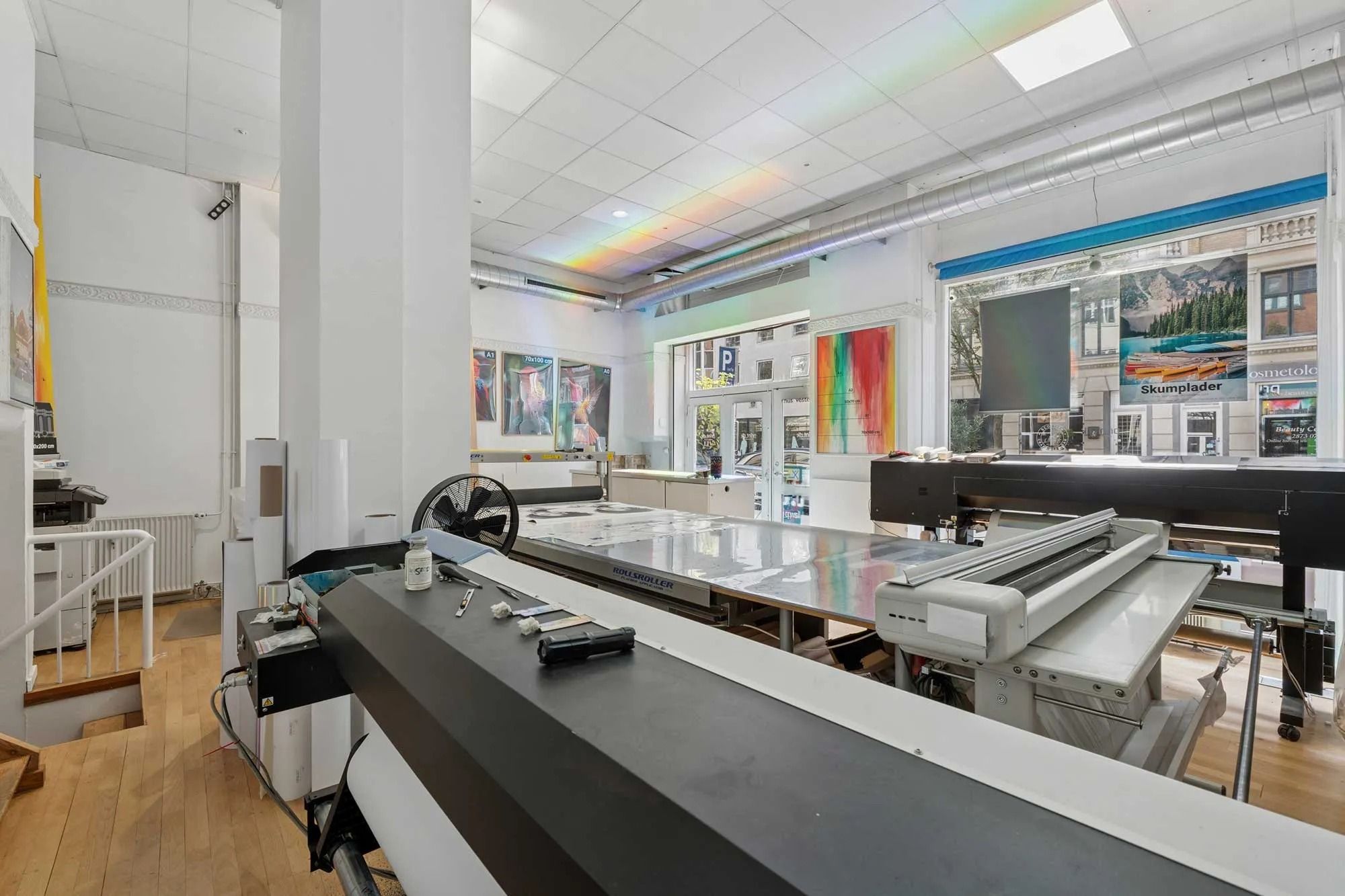 Inde i et lokale med gulv af træ og et stort tryk- og skumlemaskine i midten, sammen med flere trykværker og et