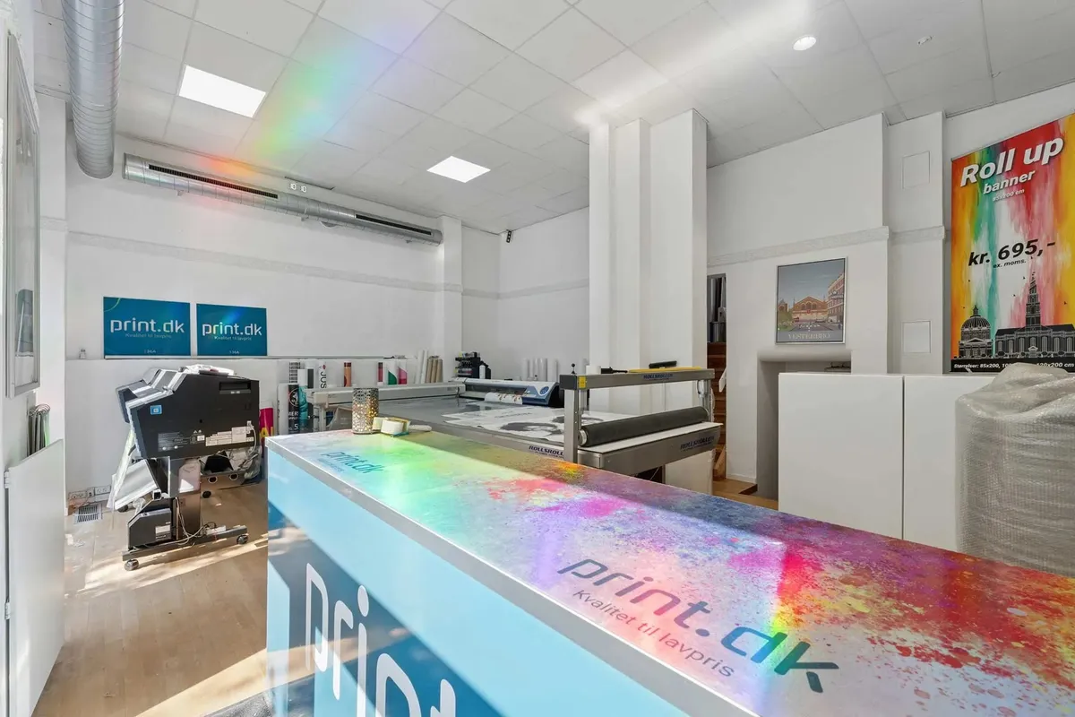 Københavns butik med print.dk-bannere på væggen, hvor en printer er placeret, og en regnbue er synlig på loftet