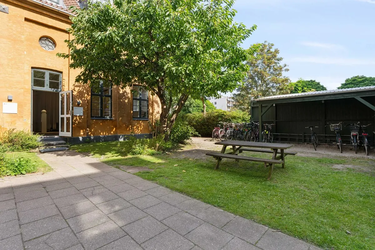 Lejlighed med grønne cykler og parkeringsplads foran træ og lysegul bygning med åben dør og vindue