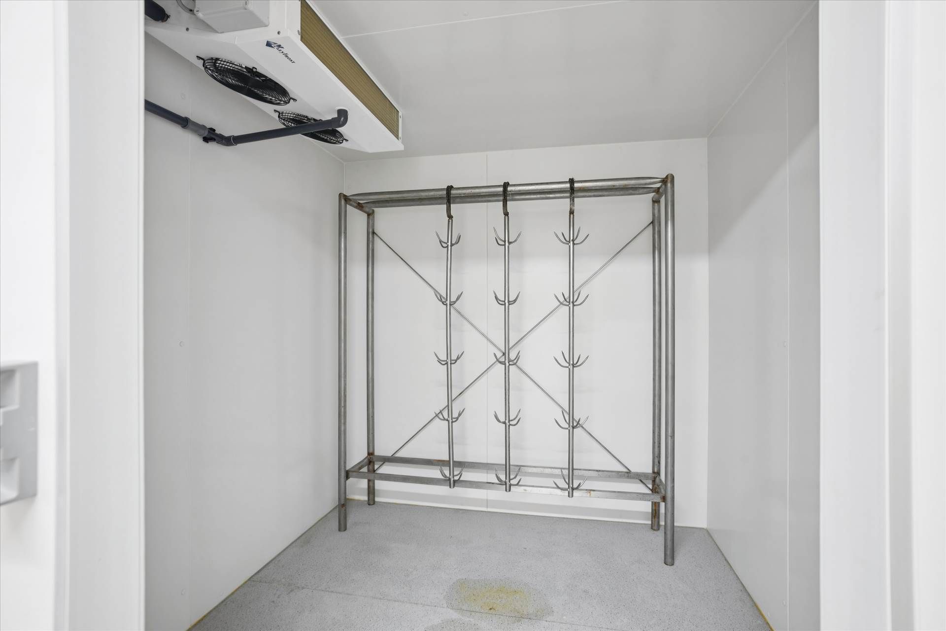 Indvendigt foto af et hvidt rum med en køleaggreg og en metalhylde med kroge til tøj. Gulvet er renset og der er et større