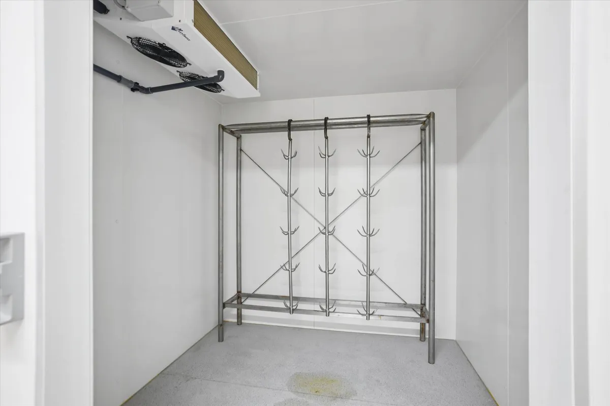 Indvendigt foto af et hvidt rum med en køleaggreg og en metalhylde med kroge til tøj. Gulvet er renset og der er et større