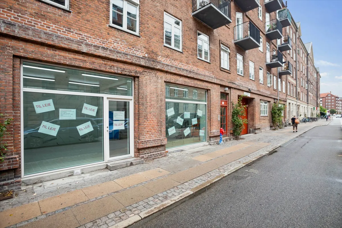 Erhvervslejemål med udsigt til gaden, hvor der er skrift på vinduet, og en person går på fortovet.
