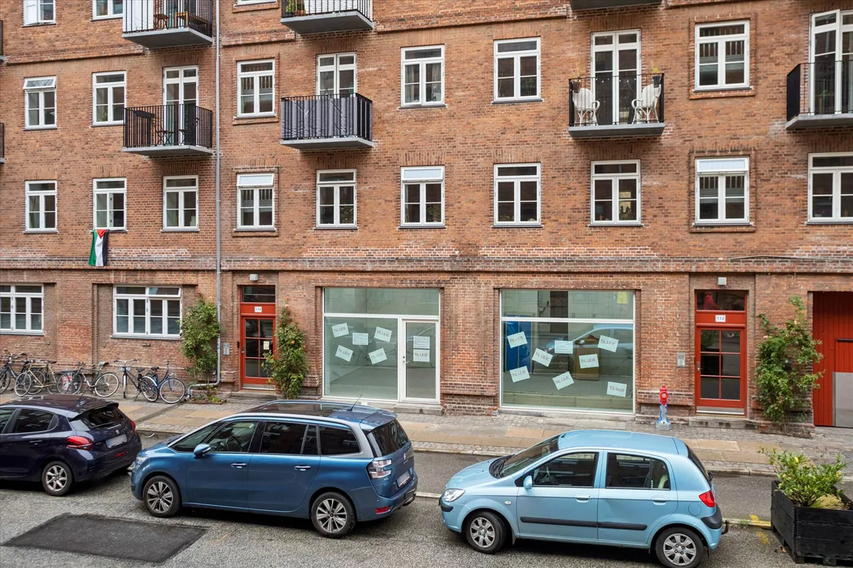 Rødt murstenshus med flere lejligheder, to biler parkeret og flere cykler foran døren