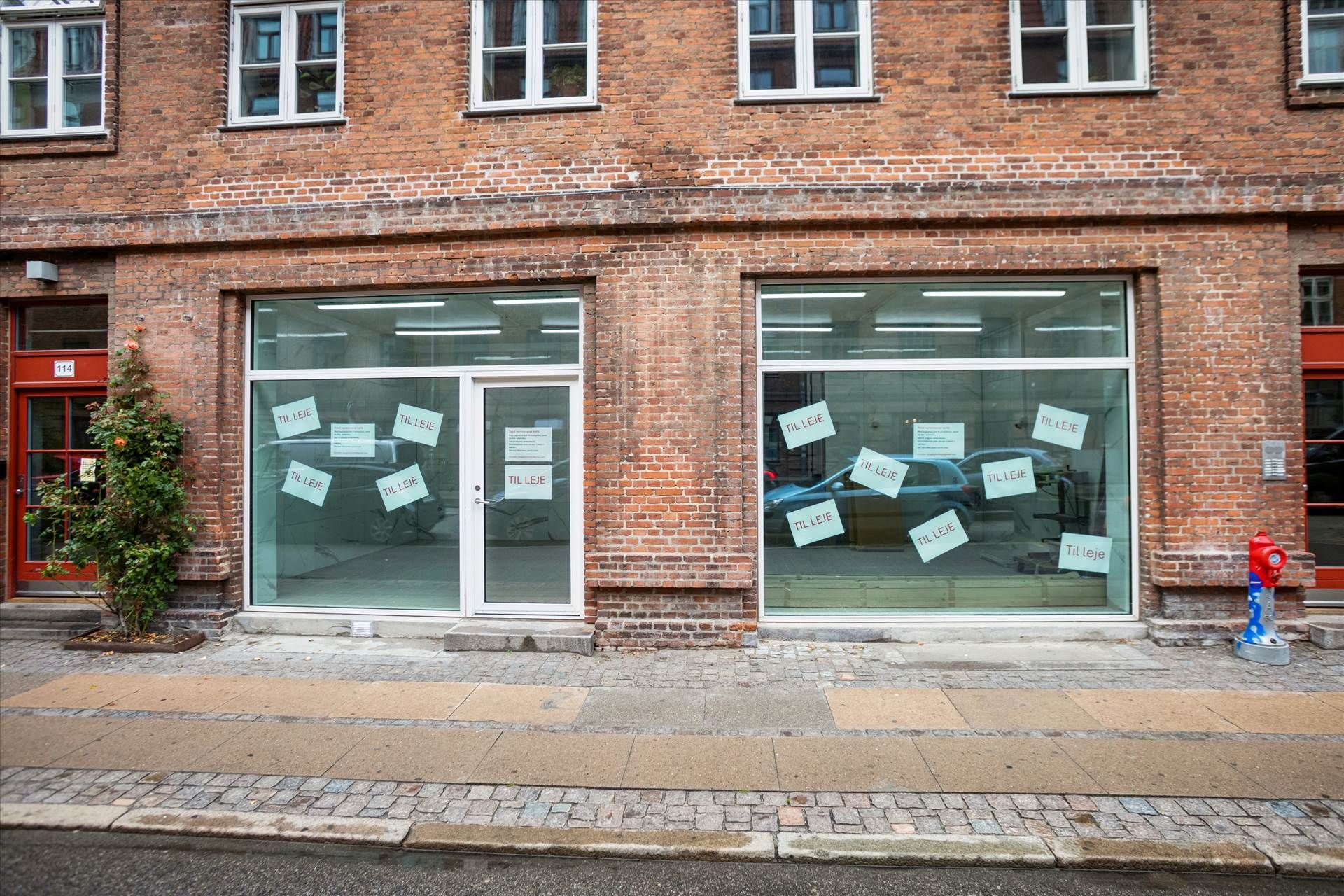 Københavnsgade med røde brandvandsslanger og en fredelig facade med røde vinduer og hvide indramninger og et skrift på