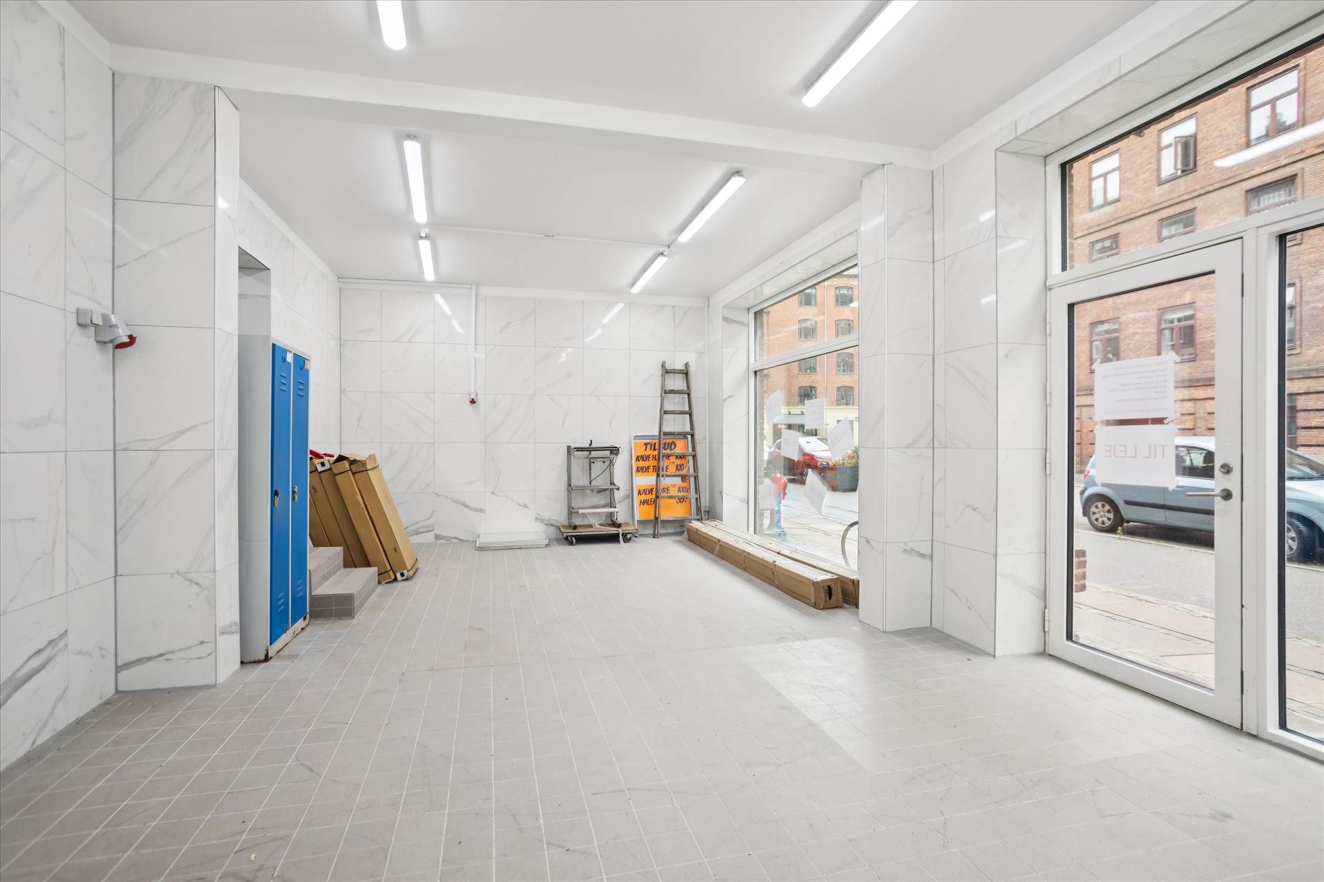 Lokaler med marmorbeklædning og hvide lofter til udlejning med vinduer og døre mod gade med biler og bygninger
