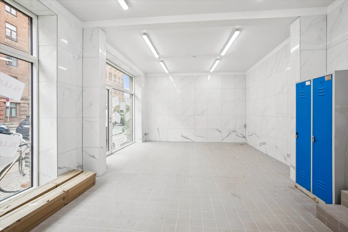 Erhvervslejemål med marmorfliser og store ruder mod gaden med cykel og bil i baggrunden