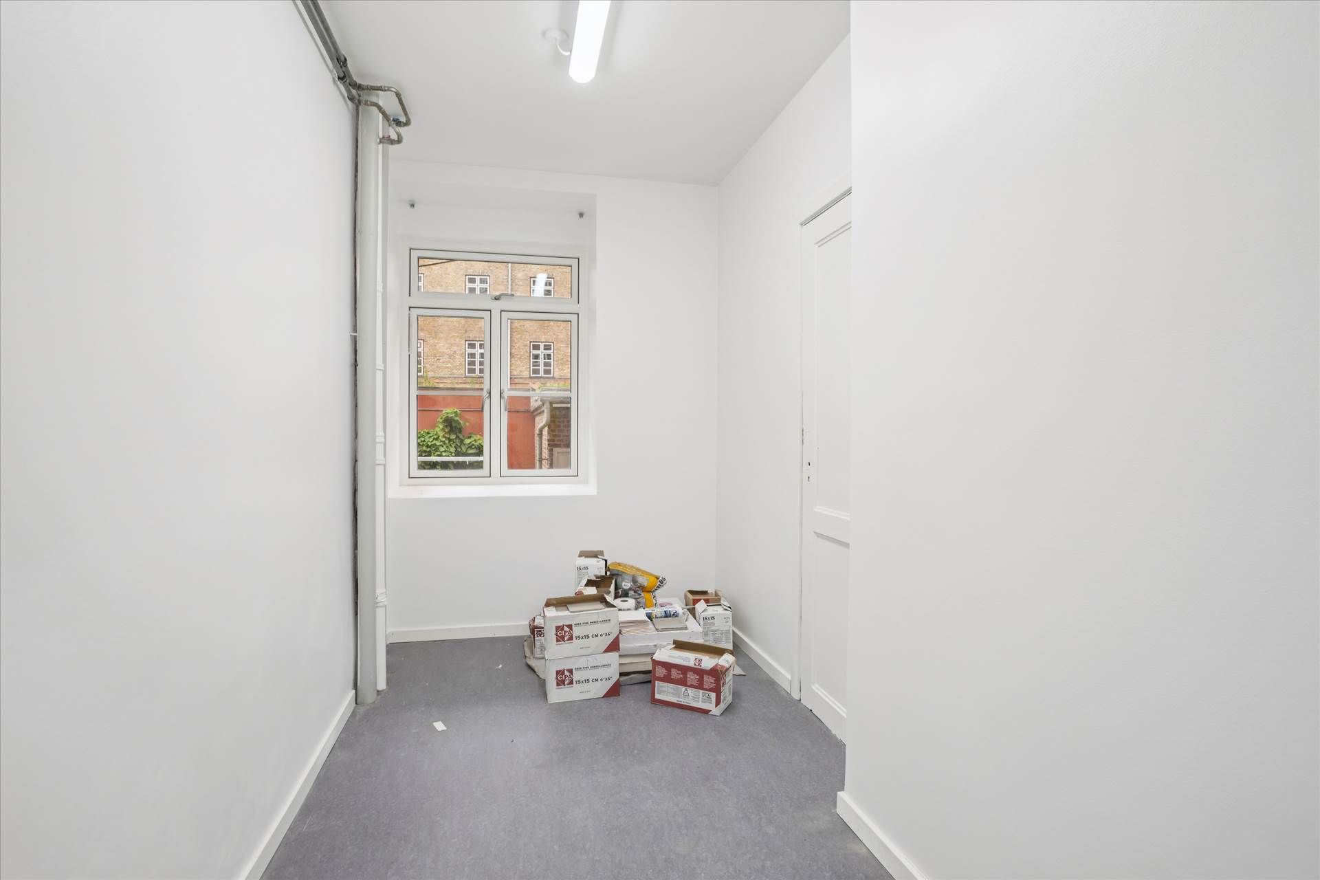 En tom gang med hvide vægge og gulv samt flere kasser med forskellige indhold samt en åben vindue