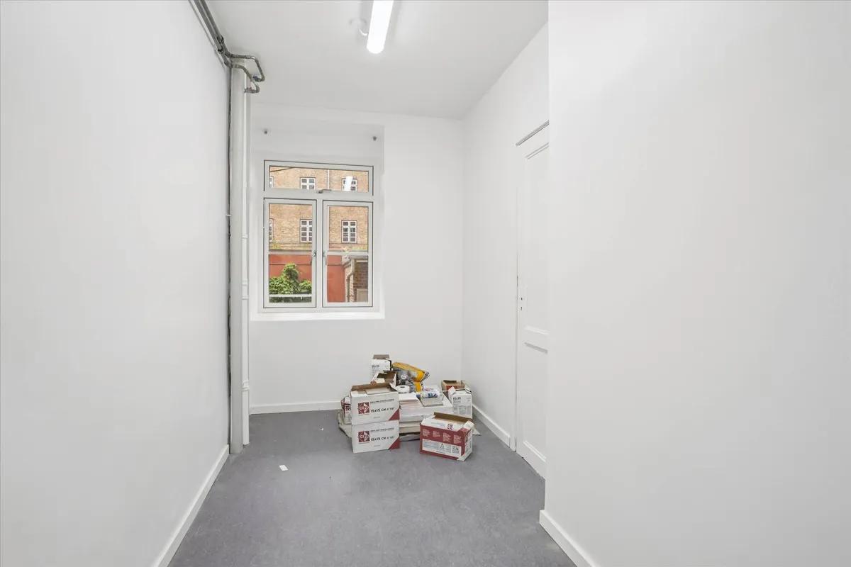 En tom gang med hvide vægge og gulv samt flere kasser med forskellige indhold samt en åben vindue