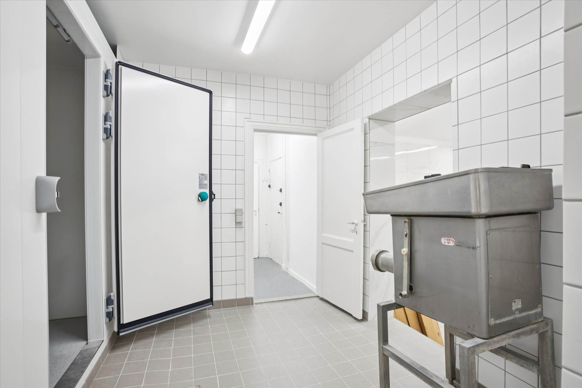 Hvidt kommercielt kølekammer med åben dør og stel til stålkomponenter samt to hvide døre med håndtag