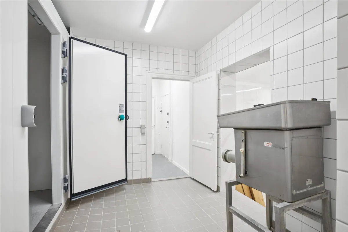 Hvidt kommercielt kølekammer med åben dør og stel til stålkomponenter samt to hvide døre med håndtag